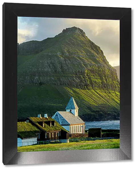 Vidareidi church and grass roof houses framed by majestic mountains of Bordoy island, Vidoy Island, Faroe Islands