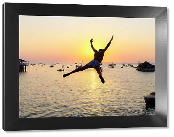 Cheerful young man jumping into the sea at sunset, Stone Town, Zanzibar, Tanzania