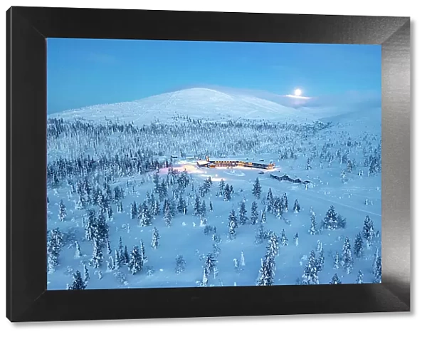 Ski area nearby a frozen snowy forest lit by moon at blue hour, aerial view, Yllastunturi National Park, Pallas, Lapland, Finland