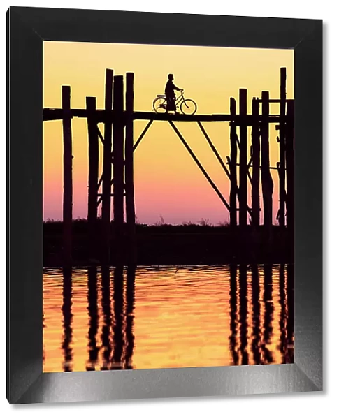 Silhouette of a person with a bicycle walking on the U-Bein wooden teak bridge at sunset, Taungthaman Lake, Amarapura, Mandalay, Myanmar