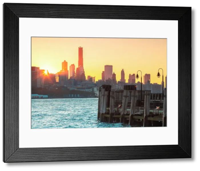 Framed Print : USA, New York City, view of the sun rising behind the buildings of Lower Manhattan with an old pier in Jersey city in the foreground Framed Print : USA, New York City, view of the sun rising behind the buildings of Lower Manhattan with an old pier in Jersey city in the foreground