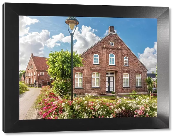 Historic brick house and lush floral decorations in the village of Rysum, Krummhoern, East Frisia, Lower Saxony, Germany