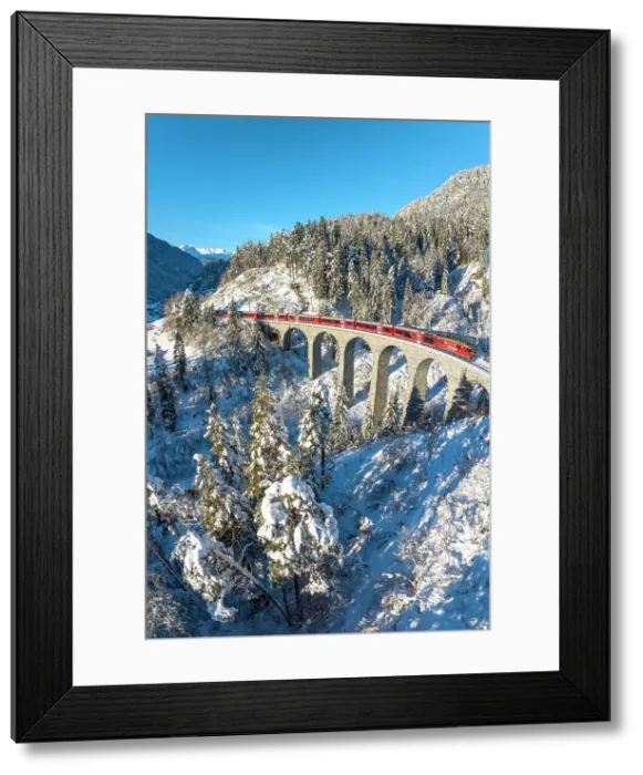 Framed Print : Red train crossing a viaduct in the fairy tale snowy landscape under a clear winter sky, Graubunden canton, Switzerland Framed Print : Red train crossing a viaduct in the fairy tale snowy landscape under a clear winter sky, Graubunden canton, Switzerland