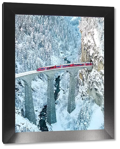 Train on Landwasser viaduct entering in a tunnel carved into a snowy mountain ridge, Filisur, Graubunden canton, Switzerland