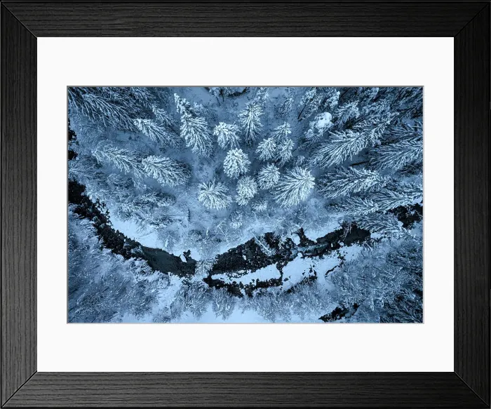 Framed Print : Aerial view of an icy river flowing along a winter snowy forest at dusk, Graubunden canton, Switzerland