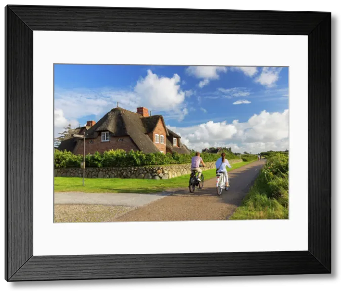 Framed Print : People cycling past traditional thatched house, Kampen, Sylt, Schleswig Holstein, Germany Framed Print : People cycling past traditional thatched house, Kampen, Sylt, Schleswig Holstein, Germany