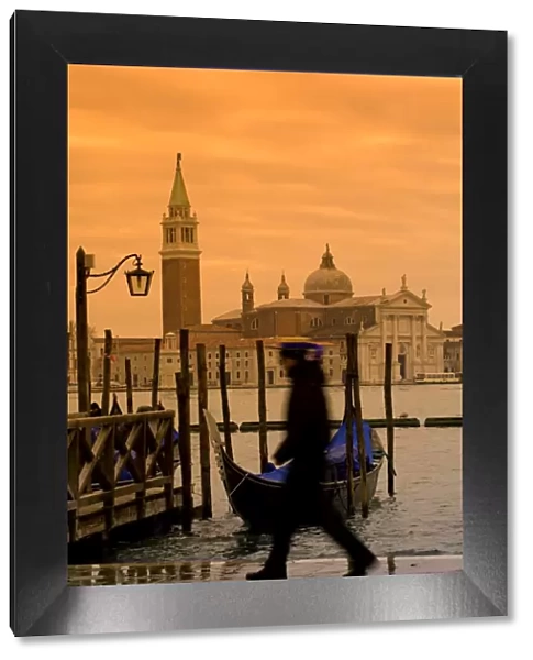 Venice, Veneto, Italy; A gondolier walking on the bacino di san marco onlooking San Giorgio Maggiore
