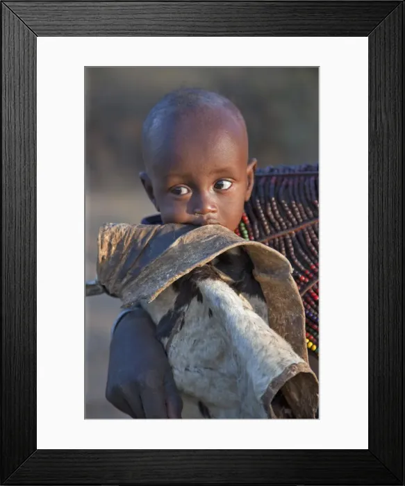 Framed Print : A Pokot child wrapped in a goatskin in his mothers arms. The Pokot are pastoralists speaking a Southern Nilotic language Framed Print : A Pokot child wrapped in a goatskin in his mothers arms. The Pokot are pastoralists speaking a Southern Nilotic language