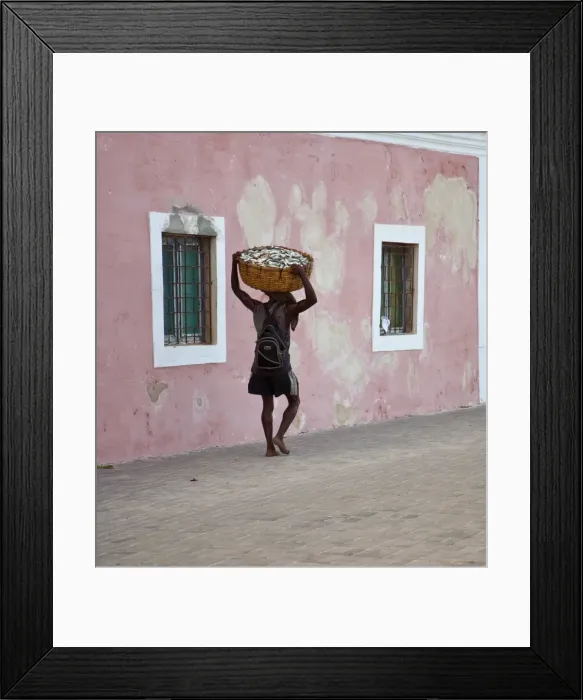Framed Print : Mozambique, Ihla de Mozambique, Stone Town. A man walks with his catch through the brightly-painted buildings Framed Print : Mozambique, Ihla de Mozambique, Stone Town. A man walks with his catch through the brightly-painted buildings