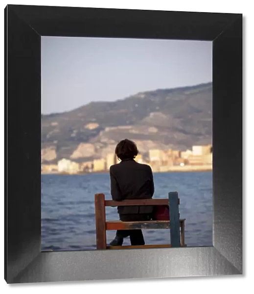 Sicily, Italy, Western Europe; A person sitting on a bench facing the fishing port of Trapani