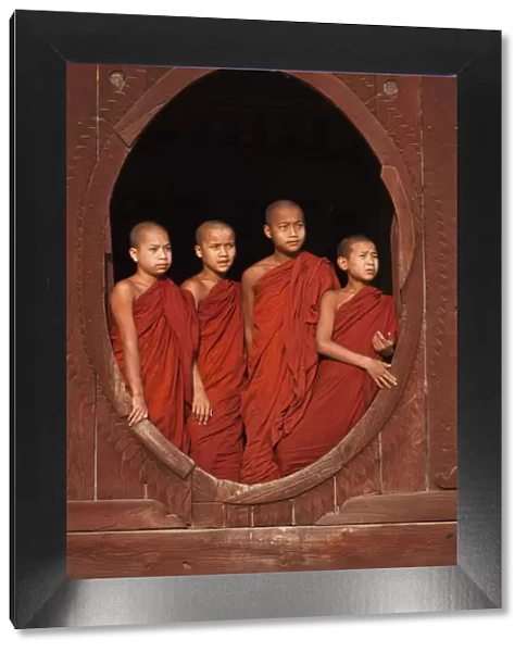 Myanmar, Burma, Nyaungshwe. Young novice monks standing at a wooden oval window