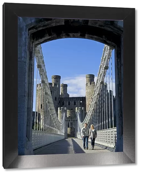UK, North Wales; Conwy. Couple on the elegant Suspension Bridge built by Thomas Telford across the Conwy River to the imposing