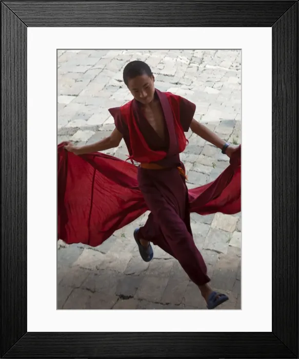 Framed Print : A young monk holds his red robes as he runs across the courtyard of Wangdue Phodrang Dzong