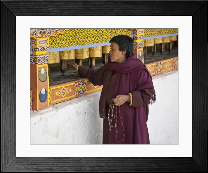 Framed Print : A woman, prayer beads in hand, spins brass prayer wheels as she mutters an invocation to protective deities at the 18th century Chorten Kora in Framed Print : A woman, prayer beads in hand, spins brass prayer wheels as she mutters an invocation to protective deities at the 18th century Chorten Kora in