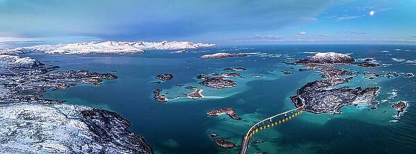 Aerial panoramic of snowcapped mountains surrounding Sommaroy island and bridge at dusk, Troms county, Norway