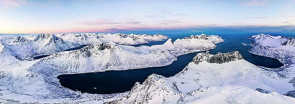 Aerial panoramic view of Grytetippen mountain covered with snow overlooking the frozen Ornfjord, Senja, Troms county, Norway