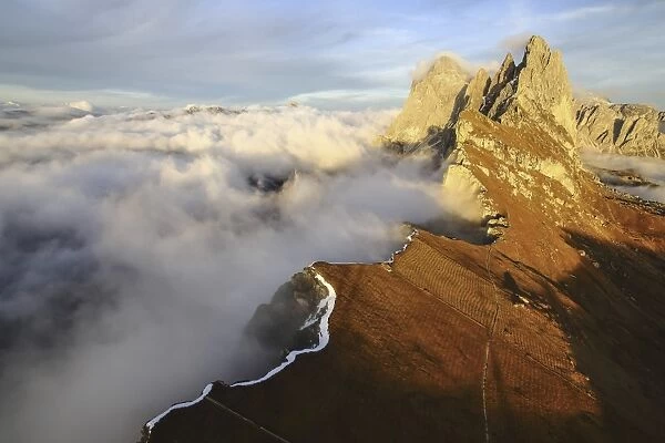 Aerial shot from Seceda of Odle surrounded by clouds at sunset