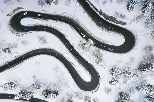 Aerial view of cars driving on narrow bends of mountain road in the snow