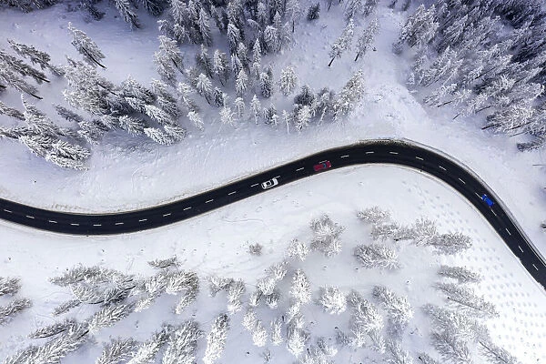 Aerial view of cars traveling on winding mountain road crossing the snow capped woods in