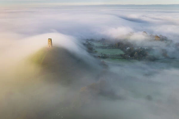 Aerial view of Glastonbury Tor shrouded in morning mist, Glastonbury, Somerset, England. Autumn (November) 2022