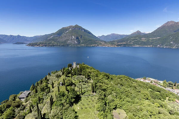 Aerial view of the green hill and castle overlooking Varenna surrounded by Lake Como