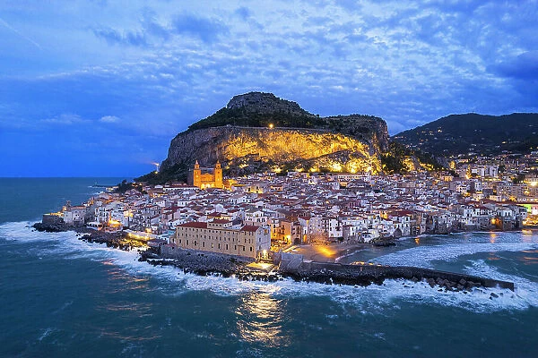 Aerial view of the illuminated Cefalu with the main cathedral and the rock behind the village, dusk time, Cefalu, Palermo province, Tyrrhenian sea, Sicily, Italy