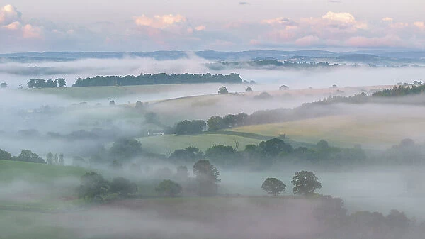Aerial view of mist shrouded countryside at dawn, Crediton, Devon, England. Summer (June) 2023