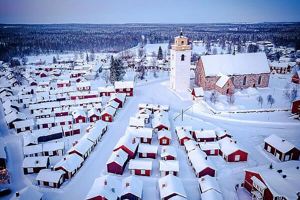 Aerial view of red cabins and church covered with snow at dusk with Lapland forest on background, Gammelstad, Lulea, Sweden