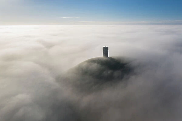 Aerial view of St Michaels Tower and Glastonbury Tor, surrounded by a sea of mist, Somerset, England. Winter (December) 2022