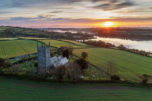 Aerial view of sunrise over the Church of St Laudus in the parish of Mabe near Falmouth, Cornwall, England. Spring (May) 2023