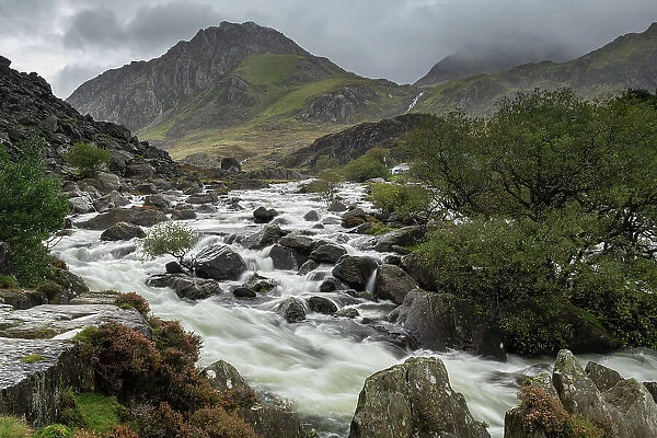 Afon Ogwen tumbling over boulder strewn riverbed with Tryfan mountain beyond, Snowdonia National Park, Wales, UK. Autumn (October) 2023