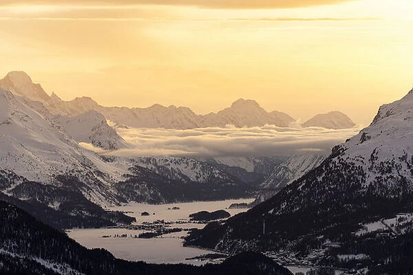 Alpine lakes of Engadine and village of Maloja covered with snow at sunset