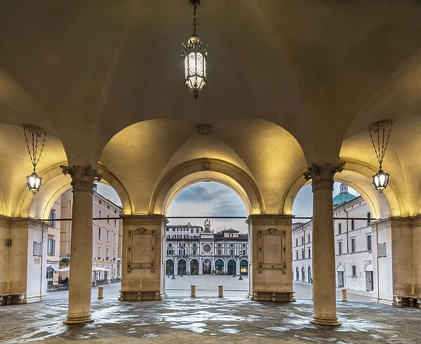 arcades with columns of the Palazzo della Loggia illuminated in the first morning, with the square in the background, Brescia, Lombardy, Italy