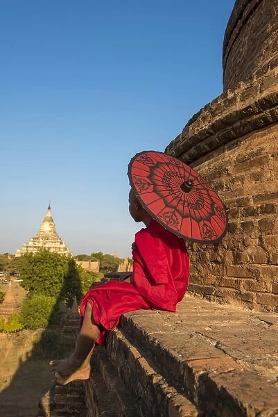 Bagan, Mandalay region, Myanmar (Burma). A young monk with red umbrella watching