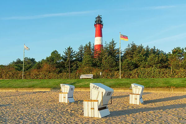 Beach chairs near German flag and Hornum lighthouse in background at sunrise, Hornum beach, Sylt, Nordfriesland, Schleswig-Holstein, Germany