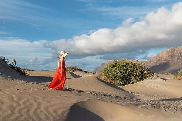 Beautiful girl with red dress walks in the sand dunes of Famara, Lanzarote, Canary Island, Spain