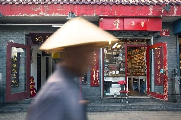 Beijing, China. Old man with conical hat passing in front of a shop in a hutong of