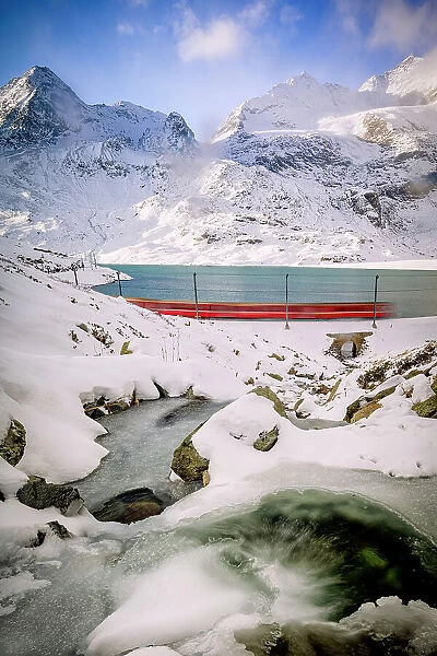 Bernina train running fast in the frozen snowy landscape nearby Lago Bianco lake, Bernina Pass, Graubunden, Engadin, Switzerland