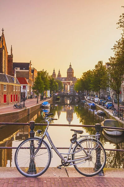A bike on a bridge with St. Nicholas church in the background at sunrise in Amsterdam