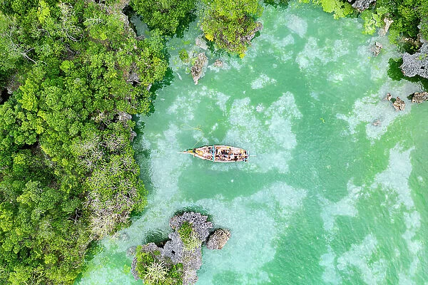 Boat sailing in the emerald green water of lagoon surrounded by mangrove forest, Kwale Island, Zanzibar, Tanzania