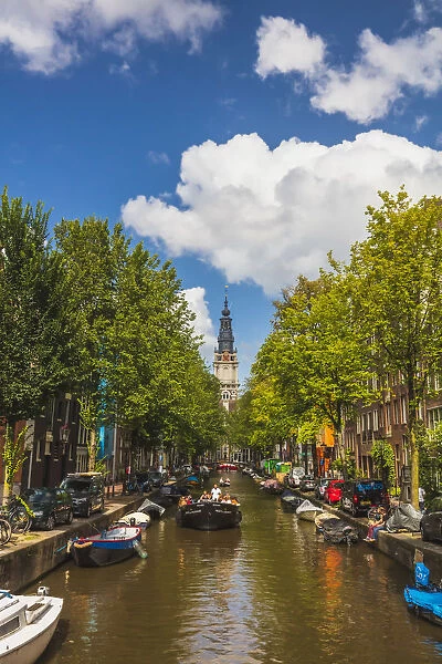 A boat with tourists with Zuiderkerk church reflecting in the water canal in Amsterdam