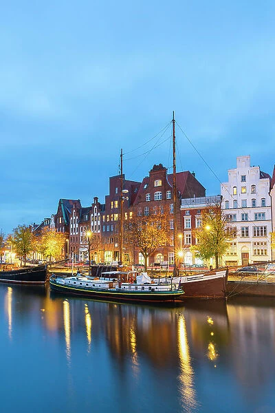 Boats anchored on Trave river and houses with traditional gables in background at twilight, Lubeck, UNESCO, Schleswig-Holstein, Germany