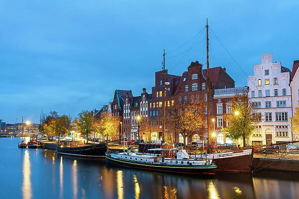 Boats anchored on Trave river and houses with traditional gables in background at twilight, Lubeck, UNESCO, Schleswig-Holstein, Germany