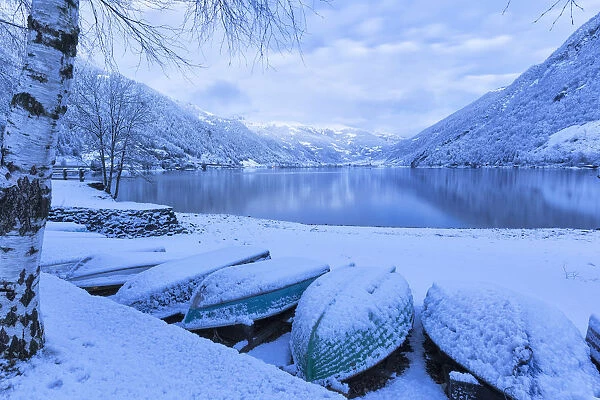 Boats covered by snow at Poschiavo Lake during twilight. Poschiavo Lake, Poschiavo Valley(Val Poschiavo), Graub√ºnden, Switzerland