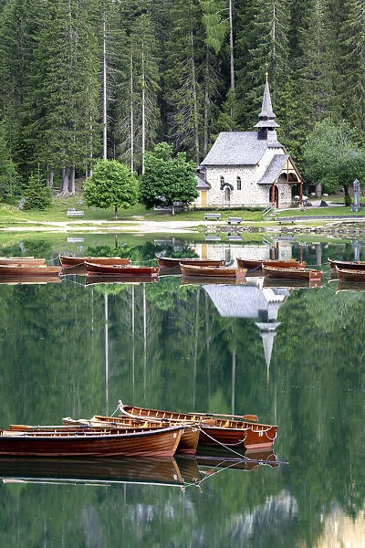 Boats moored in lake Braies (Pragser Wildsee) with small chapel and forest on background