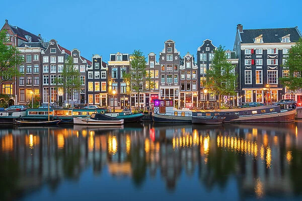 Boats moored in Singel canal near typical houses at twilight, Amsterdam, Netherlands