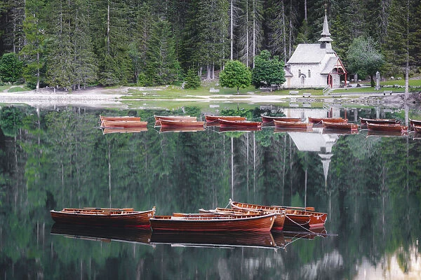 Boats in the pristine lake Braies (Pragser Wildsee) with the small chapel mirrored in