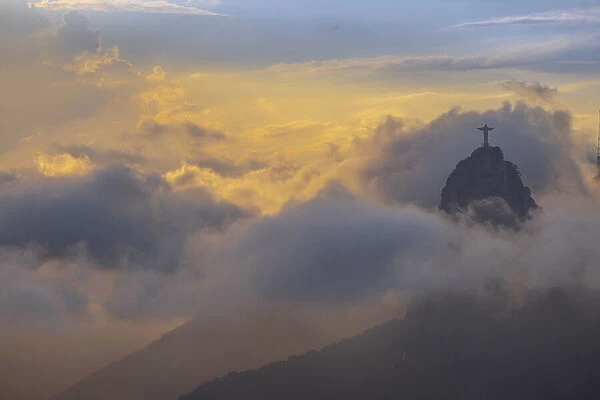 Brazil, Rio de Janeiro, Christ the Redeemer statue on Corcovado Hill surrounded by golden clouds at sundown