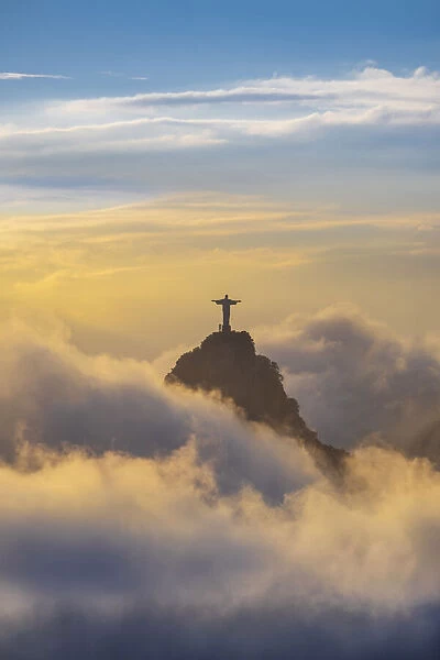 Brazil, Rio de Janeiro, Christ the Redeemer statue on Corcovado Hill surrounded by golden clouds at sundown