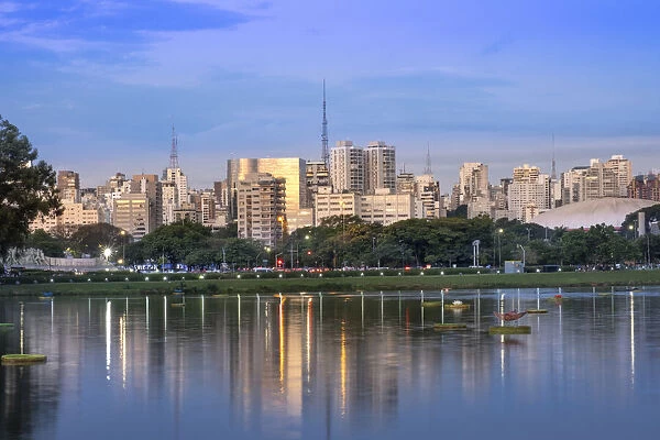 Brazil, Sao Paulo, Sao Paulo City, urban city skyline reflected in the lake in Ibirapuera Park. Copy space, no people, golden evening light